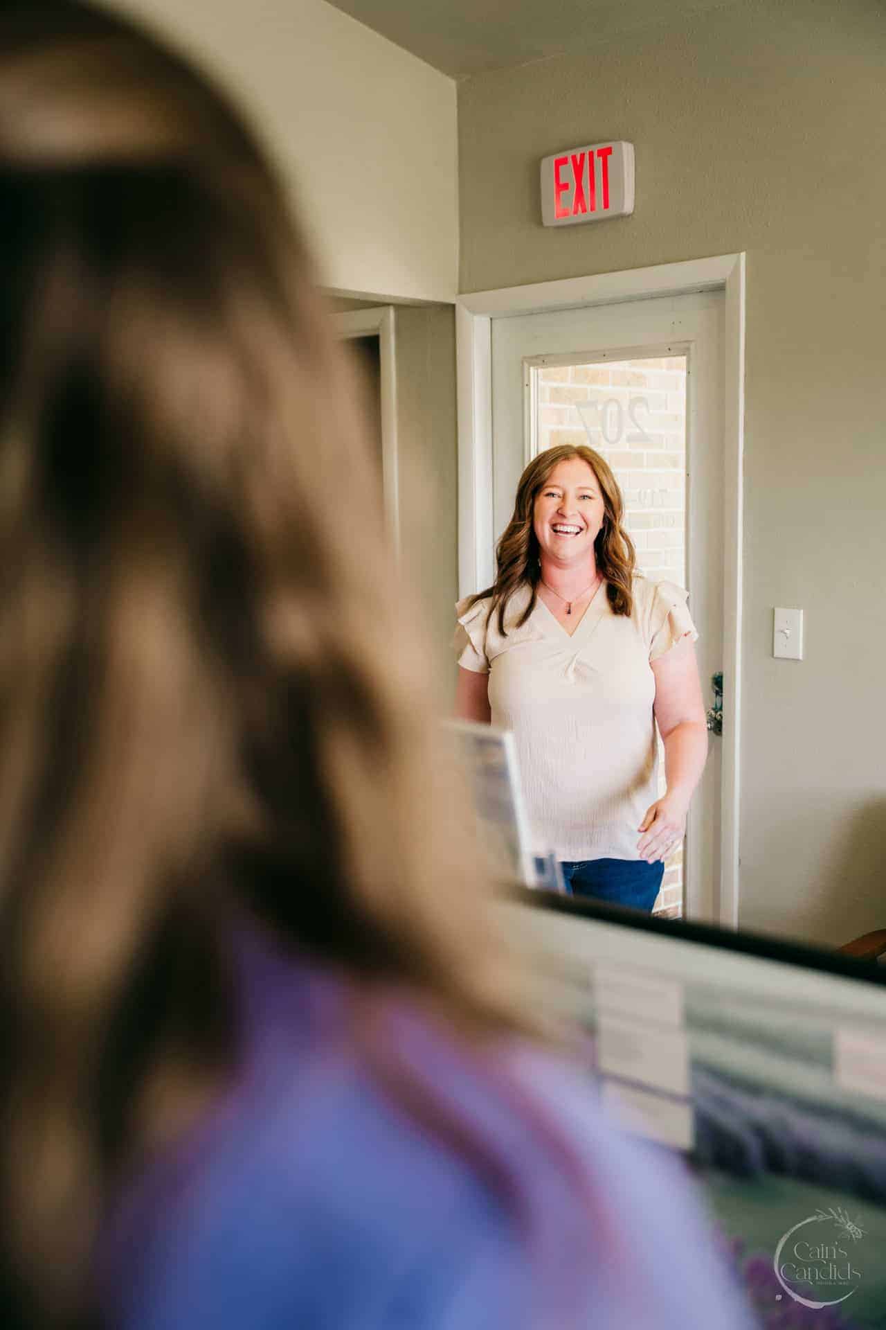 Smiling woman brushing her teeth in front of a mirror.